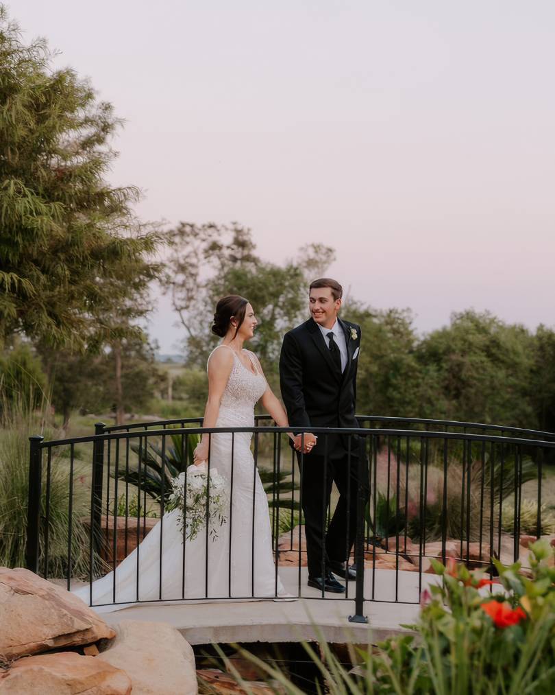 bride and groom walking across a bridge at the springs wallisville in bride's justin alexander wedding dress